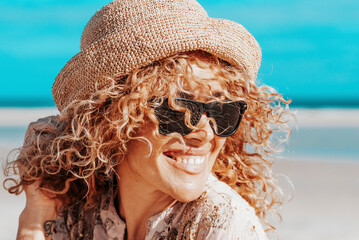Portraits of a joyful curly-haired woman with sunglasses enjoying a summer day at the beach. Happy...