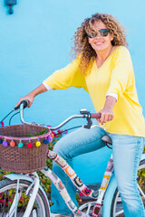 Smiling curly-haired woman in her 40s riding a city bicycle outdoors. Healthy lifestyle,...