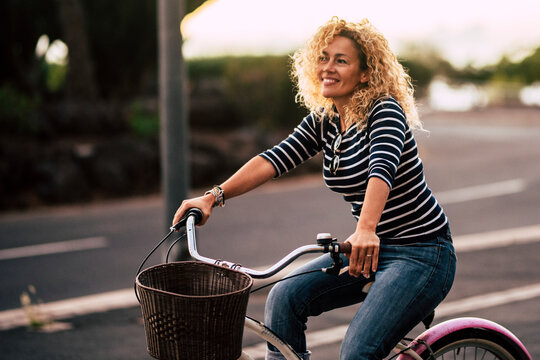 Smiling curly-haired woman in her 40s riding a city bicycle outdoors. Healthy lifestyle, eco-friendly mobility, freedom, leisure time, independence and sustainable living in an urban environment