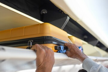 Person's hands are seen placing or retrieving a yellow hard-shell suitcase.