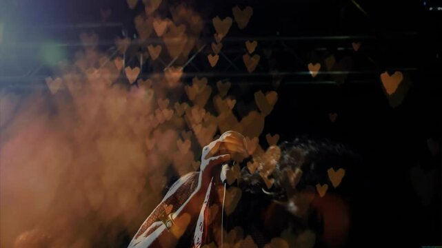 Singer holding microphone singing on music stage activating gold hearts over haze for crescendo