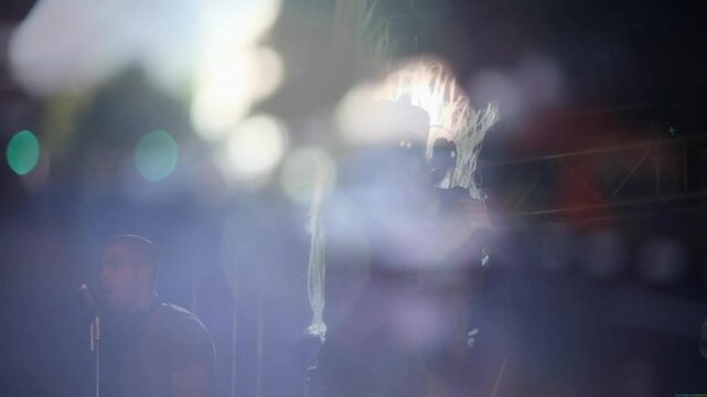Lens flare hitting singer causing hair swinging in street music gig showing bandmate singing