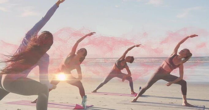 Female instructor guiding yoga group entering reverse warrior bend on beach, with smoke lens flares