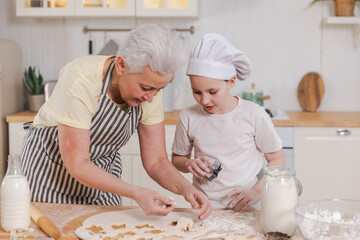 Happy family in kitchen. Grandmother granddaughter child cutting cookies of dough on kitchen table together. Grandma teaching kid girl cook bake cookies. Household teamwork helping family generations
