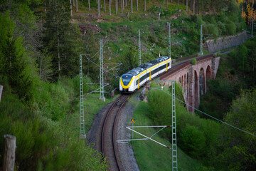 Yellow-white train goes on the old bridge aqueduct within the mountain forest