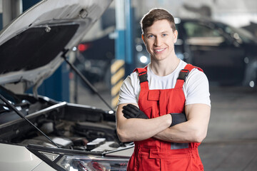 Happy man auto mechanic in red overalls standing confidently in car repair shop