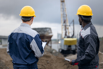 Surveying engineers caucasian and african in sand quarry assessing ore mining operations, back view