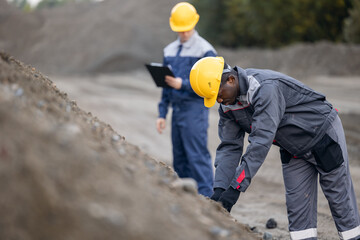 African adult male surveyor and caucasian young male engineer in sand quarry ore mining
