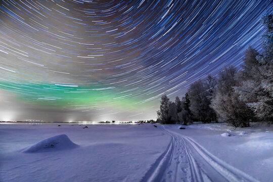 View of the mesmerizing celestial dance of stars swirling above a snow-covered landscape, kissed by the ethereal glow of the aurora borealis, Oulu, Finland.