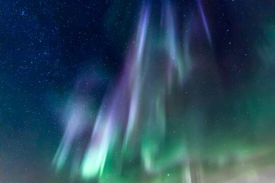 View of ethereal green and purple Northern Lights dance across the starry night sky, painting a celestial masterpiece, Rovaniemi, Finland.