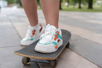 Close-up of a teenager's feet in light, casual sneakers firmly planted on a skateboard, exuding a sense of confidence, freedom, and the spirit of summer.