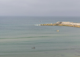 Fishing boats and paddle board near coastal rocks in ocean