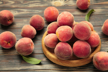 Sweet peaches and leaves on wooden plate on brown background. Space for text