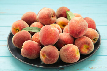 Sweet peaches and leaves on dark plate on blue wooden background.