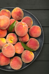 Sweet peaches and leaves on dark plate on black wooden background. Vertical photo