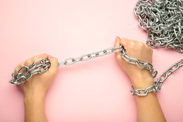 Hands are chained in chains on pink background. Space for text