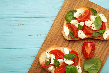 Tasty sandwich with mozzarella cheese, tomatoes and basil on cutting board on blue wooden...