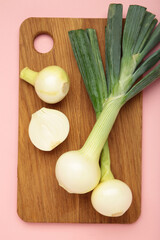 Green onion on cutting board on pink background. Vertical photo