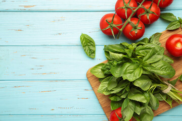 Fresh cherry tomatoes with basil leaves on blue wooden background. Space for text