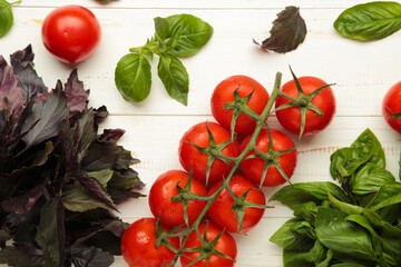 Fresh cherry tomatoes with basil leaves on white wooden background