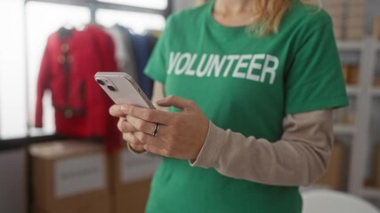 Woman holds smartphone while texting at a donation center as a volunteer in a warehouse charity wearing a shirt with visible rings and blonde hair. - Powered by Adobe