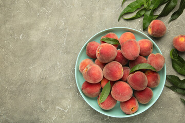 Sweet peaches and leaves on mint plate on grey concrete background. Space for text