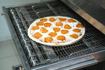 A freshly made pizza with orange toppings is placed in a pizza oven. 