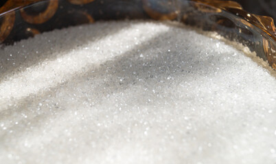 White sugar in a yellow glass vessel under sunlight closeup