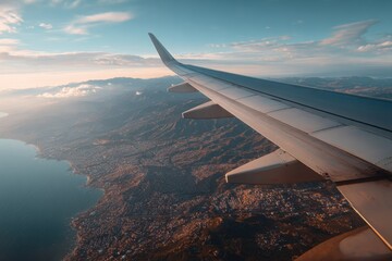 Obraz premium Stunning aerial view from an airplane wing showcasing a beautiful landscape with mountains and coastline during sunset