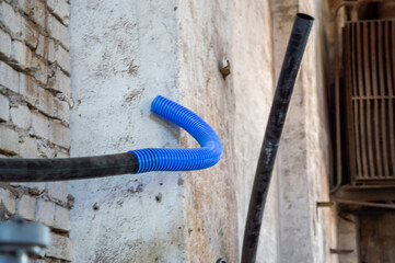 A curved blue hose connects to a dark pipe against a weathered wall in a warehouse, showcasing...