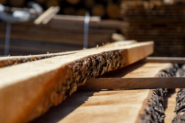 Sunlight highlights the textures and imperfections of wooden planks stacked in a lumberyard,...