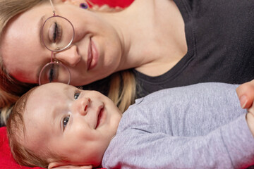 Mother looks with tenderness at her smiling newborn son lying next to her. Horizontally. 