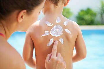 Mother applying sunscreen in sun shape on child's back near pool