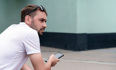 Young man with sunglasses resting on his head, wearing a casual white t shirt, holding a smartphone...