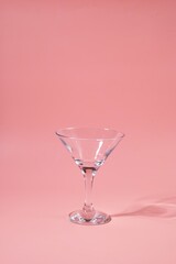 Empty triangular martini or cocktail glass on pink plain background.