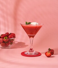 Non-alcoholic strawberry cocktail with ice cream scoop in triangle martini glasses on plain pink background. Valentine's day concept.