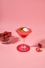Non-alcoholic strawberry cocktail with ice cream scoop in triangle martini glasses on plain pink background. Valentine's day concept.