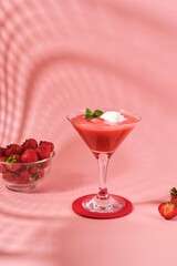 Non-alcoholic strawberry cocktail with ice cream scoop in triangle martini glasses on plain pink background. Valentine's day concept.