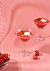 Non-alcoholic strawberry cocktail with ice cream scoop in triangle martini glasses on plain pink background. Valentine's day concept.