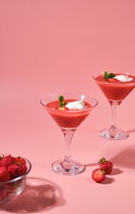 Non-alcoholic strawberry cocktail with ice cream scoop in triangle martini glasses on plain pink background. Valentine's day concept.