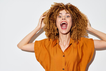 excited woman with curly hair expressing joy, vibrant healthy energy, wearing an orange top against...