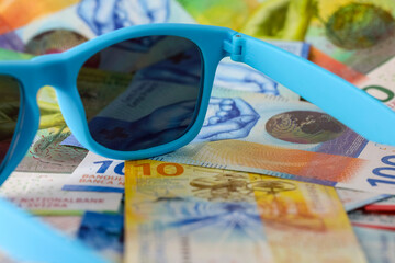 Sunglasses lying on Swiss franc banknotes