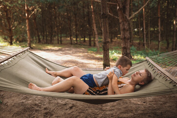Emotional Mother and son are fooling around in hammock in summer forest. Family outdoor recreation,...