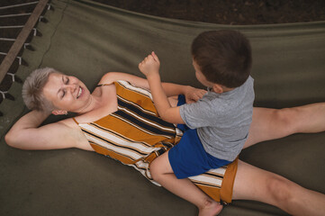 Mother and son are relaxing in the forest in a hammock in the summer. Family outdoor recreation,...
