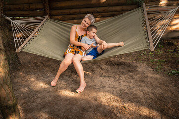 Emotional Mother and son are fooling around in hammock in summer forest. Family outdoor recreation,...