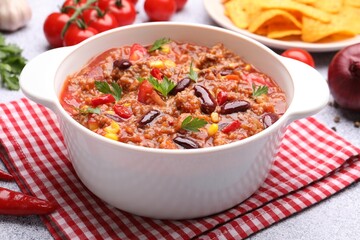 Tasty chili con carne in bowl, nachos and ingredients on grey table, closeup