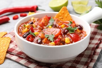 Tasty chili con carne in bowl and nachos on grey textured table, closeup