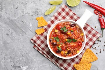 Tasty chili con carne in bowl and nachos on grey textured table, flat lay. Space for text