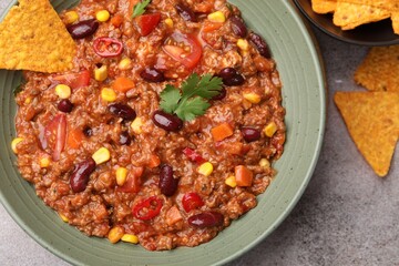 Tasty chili con carne in bowl and nachos on grey table, flat lay