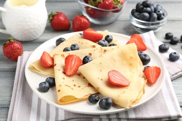 Delicious crepes with berries and cream on grey wooden table, closeup